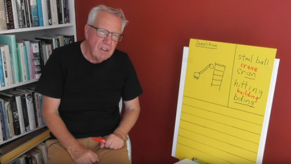 Man sitting on chair next to flip chart with images and writing on it
